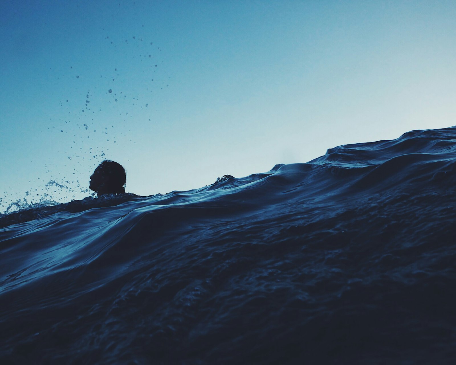 夕暮れの水面から顔を出して息を継ぐ人のシルエット